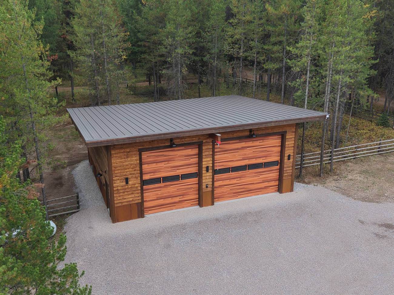 The finished garage from the air, single-pitch roof and gravel apron cut into the forest