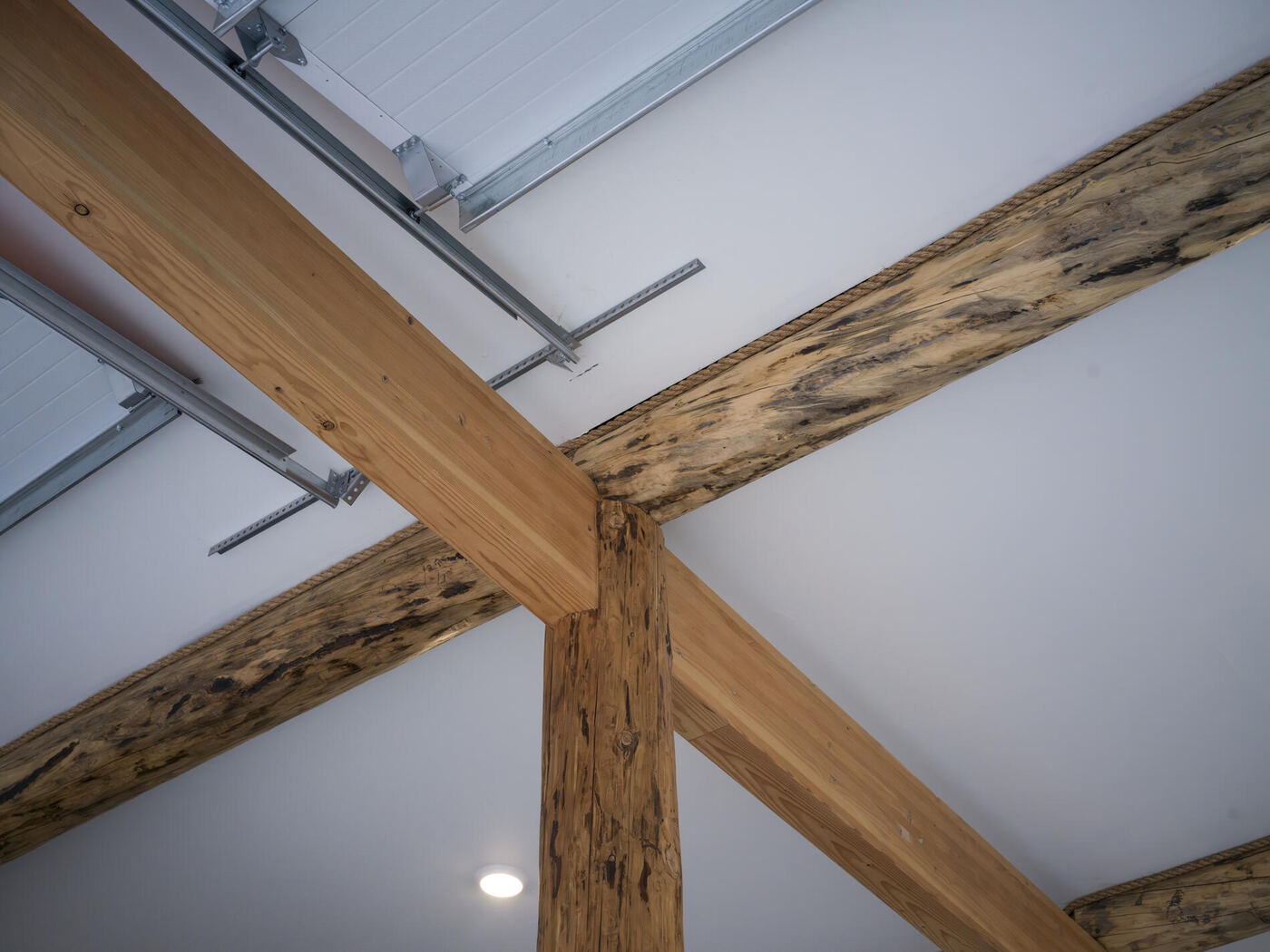 A timber post meeting crossing beams beneath a white ceiling