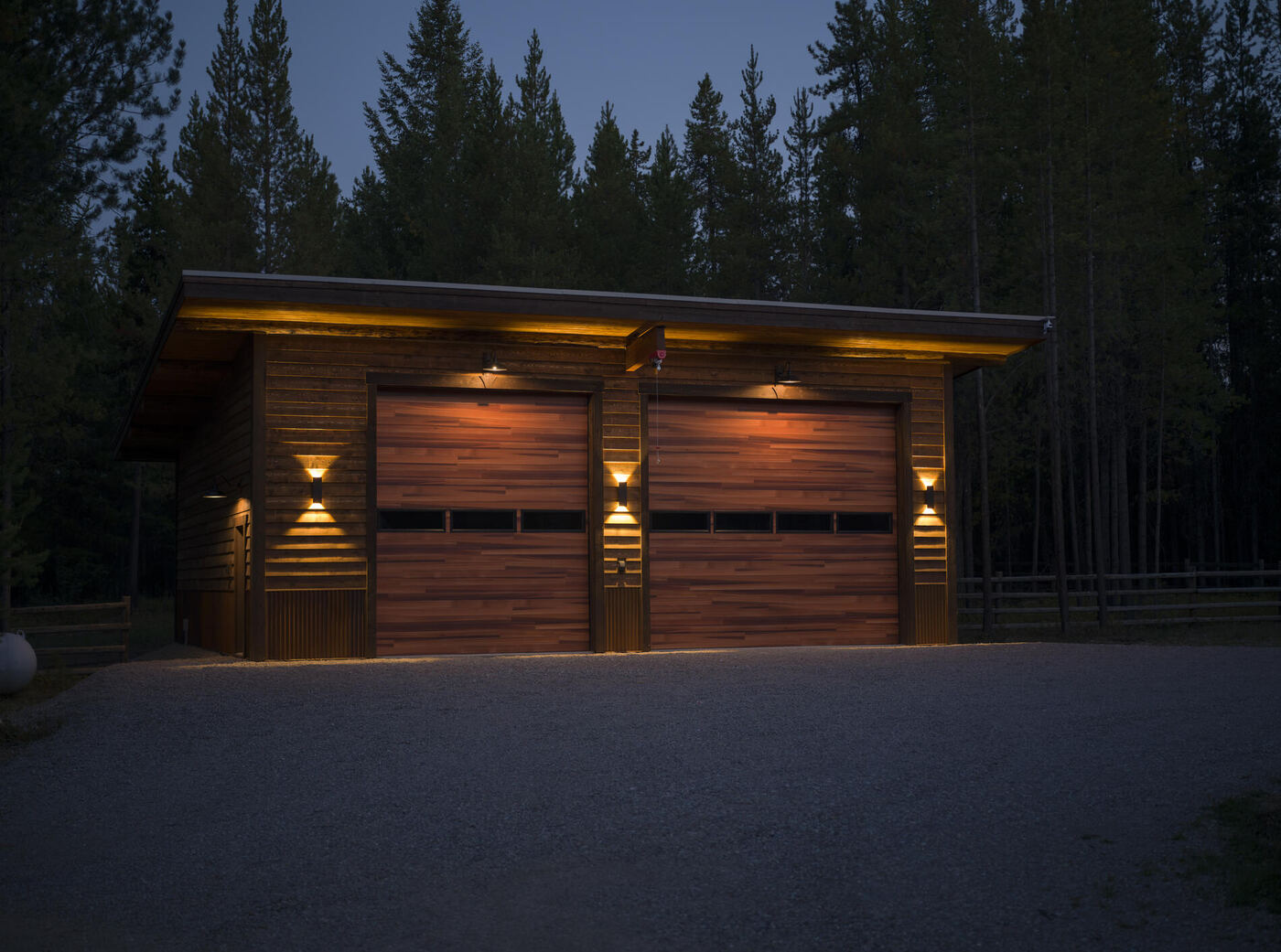Two-bay timber garage at dusk with the exterior lights on