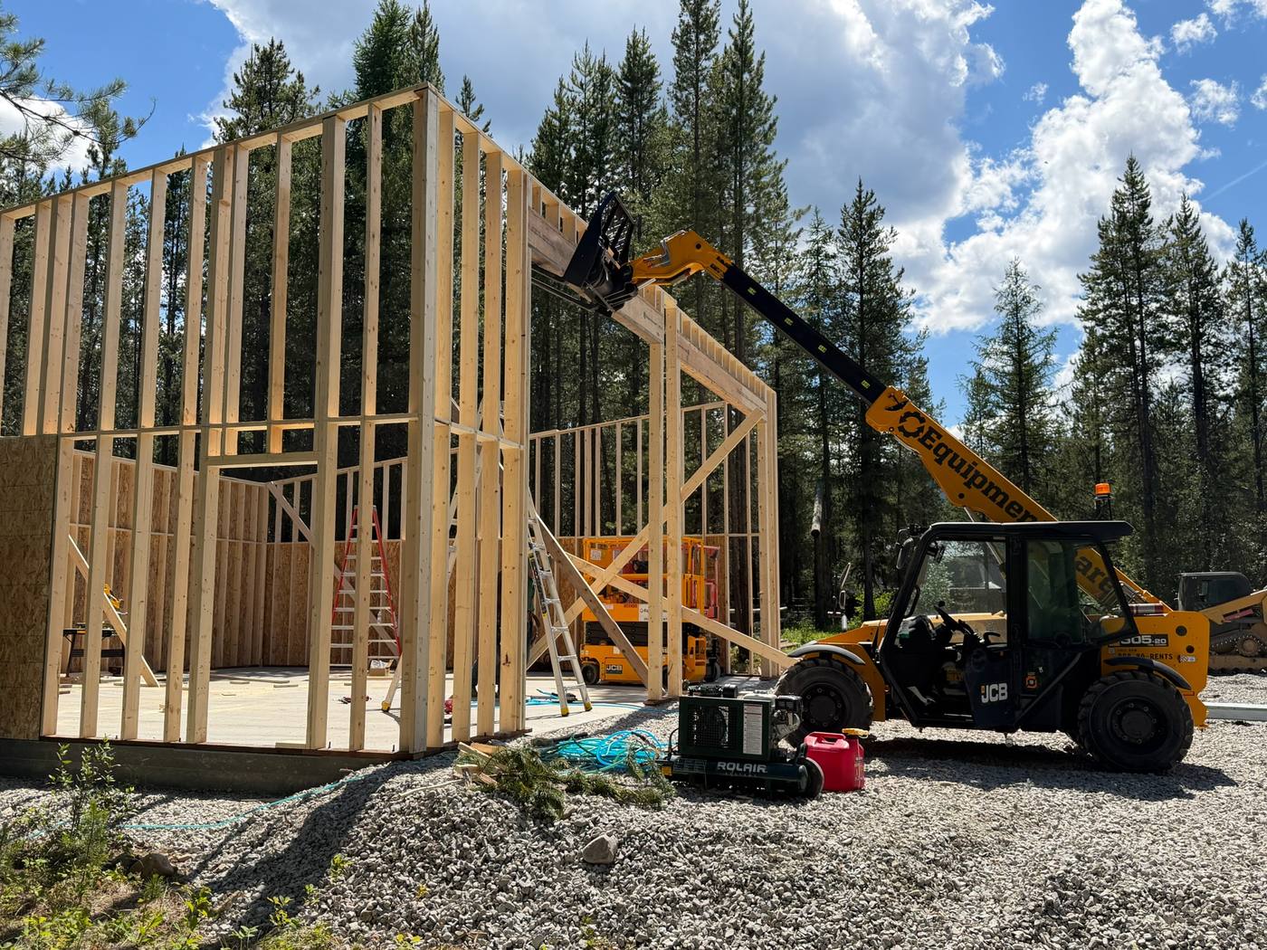 Framed walls standing on the finished pad with a telehandler alongside