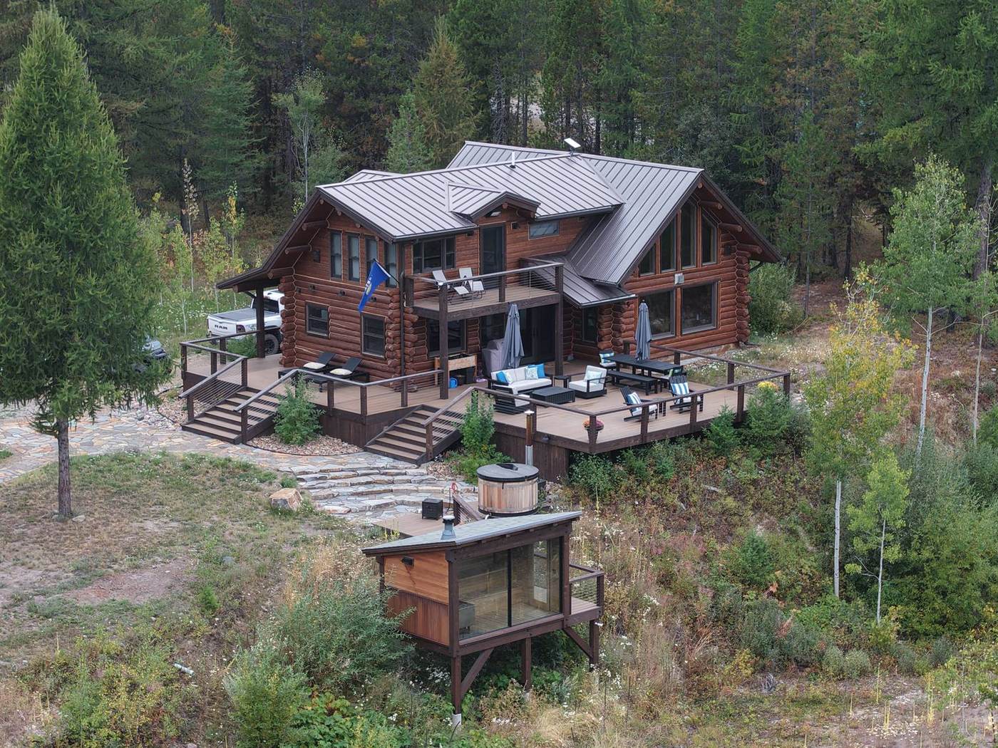 Aerial of the cabin, deck, hot tub and sauna on a cleared bench in the forest