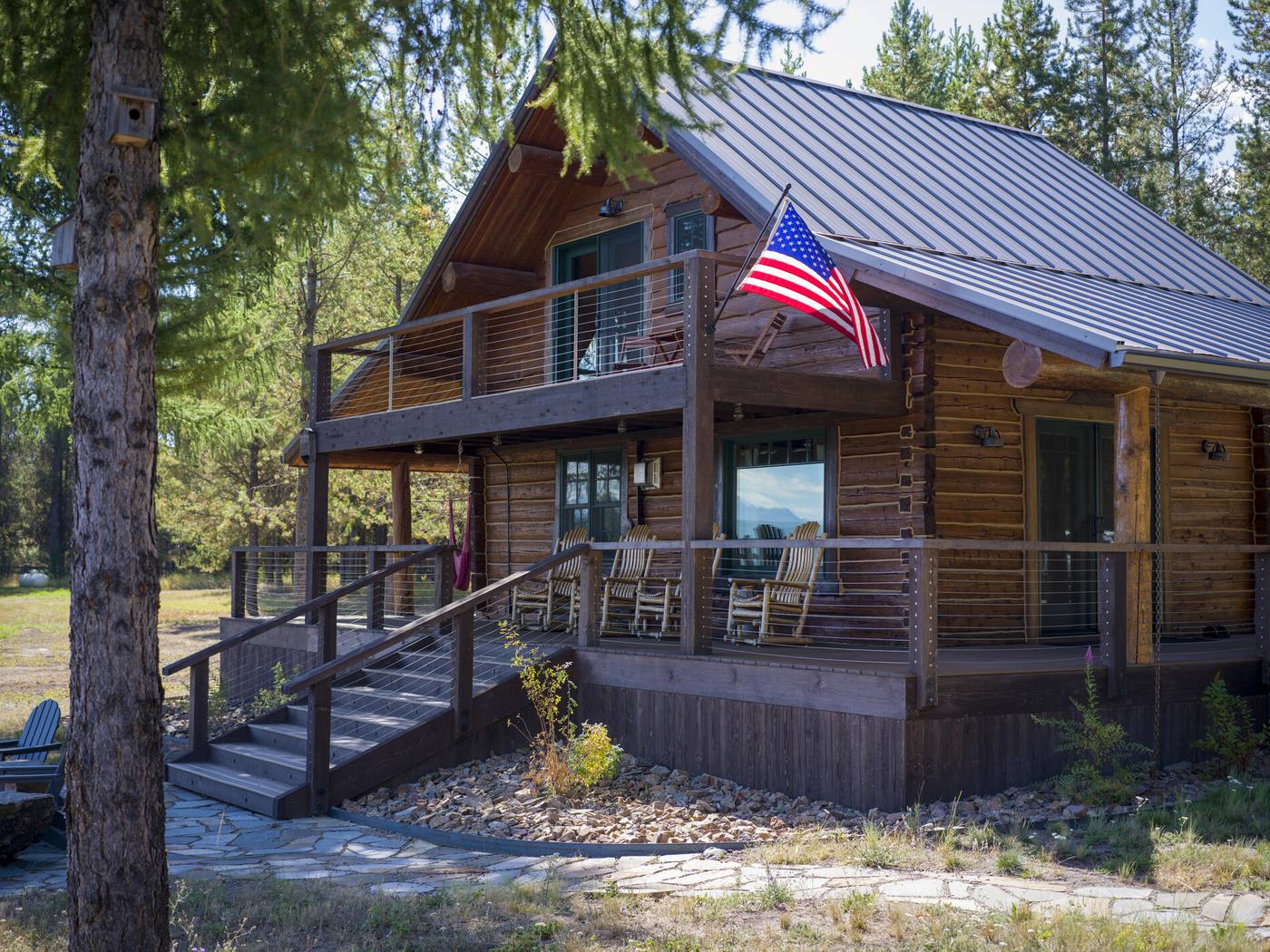 Log cabin with a metal roof, deck and flag, forest behind