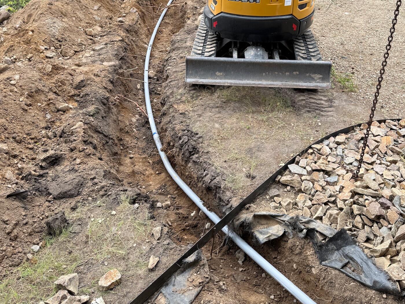 An open utility trench with the water line laid in and drain rock alongside